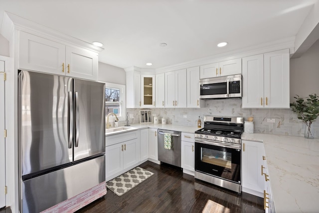 kitchen featuring dark wood-type flooring, a sink, stainless steel appliances, white cabinetry, and backsplash