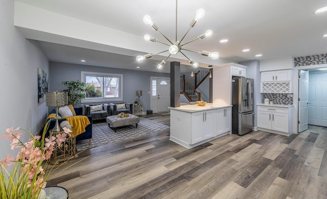 kitchen with stainless steel fridge, open floor plan, wood finished floors, light countertops, and white cabinetry