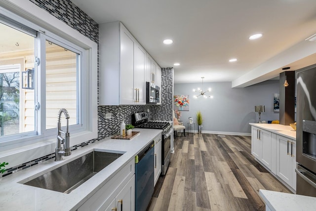 kitchen with wood finished floors, a sink, white cabinetry, appliances with stainless steel finishes, and backsplash