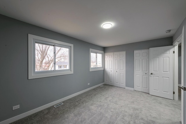 unfurnished bedroom featuring multiple closets, visible vents, carpet floors, and baseboards