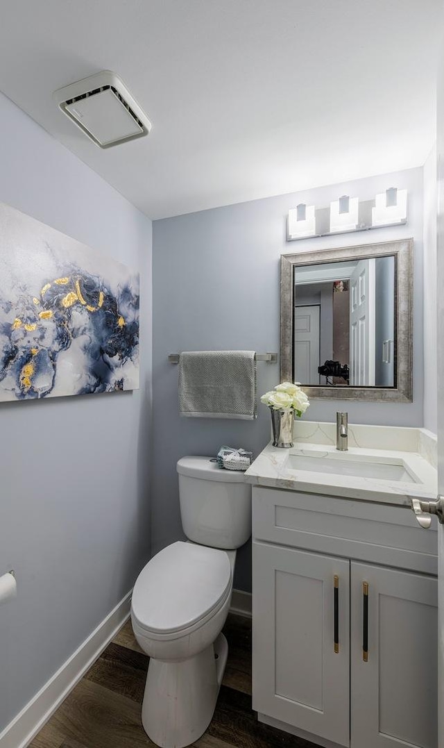 half bath with visible vents, toilet, vanity, wood finished floors, and baseboards