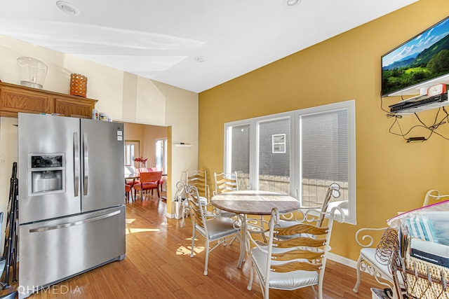 kitchen with stainless steel fridge, baseboards, lofted ceiling, brown cabinets, and light wood-type flooring