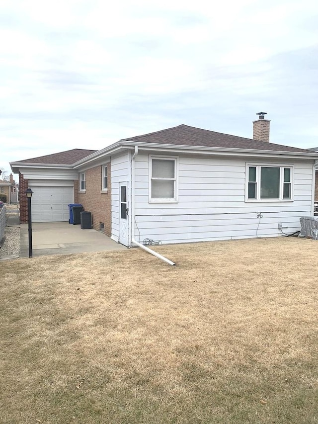 back of property featuring brick siding, a patio, a chimney, a lawn, and a garage