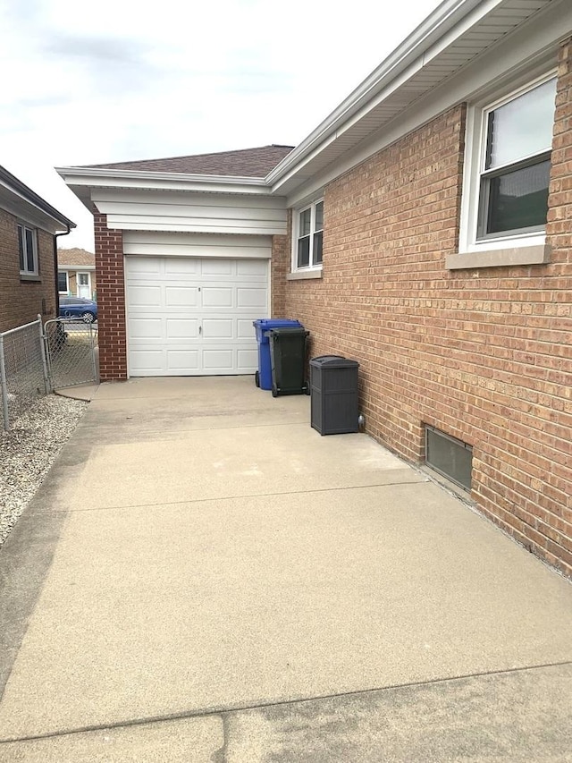 view of side of property featuring concrete driveway, brick siding, an attached garage, and fence