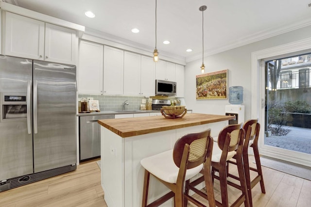 kitchen featuring crown molding, butcher block countertops, light wood-style floors, stainless steel appliances, and a sink