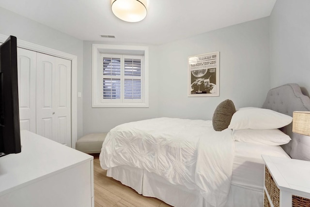 bedroom with light wood-style flooring, visible vents, and a closet