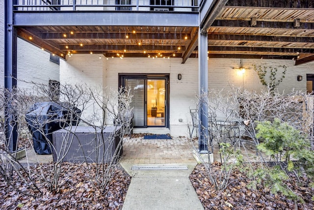 doorway to property with central air condition unit, a patio, brick siding, and a balcony