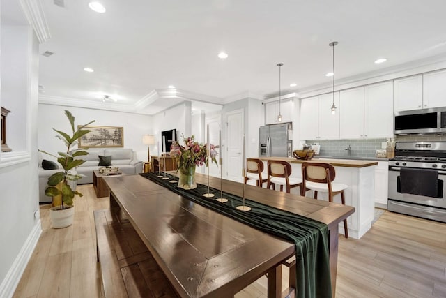 dining room with recessed lighting, crown molding, and light wood-style floors