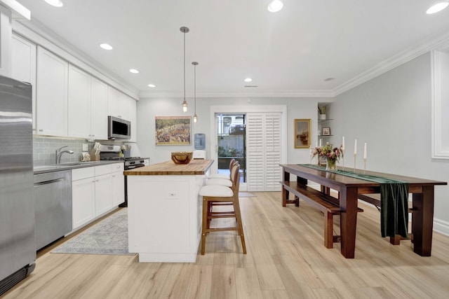 kitchen with a kitchen island, white cabinetry, appliances with stainless steel finishes, crown molding, and wooden counters