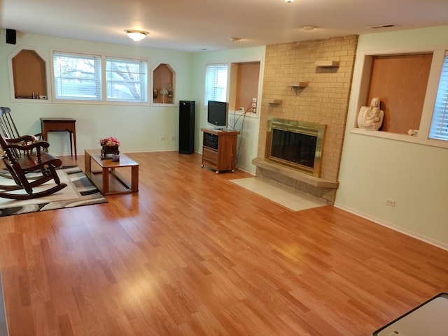 living area featuring a brick fireplace, visible vents, light wood-style flooring, and baseboards