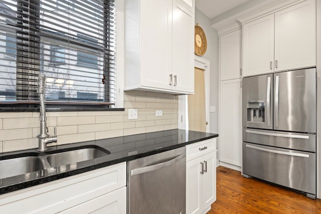 kitchen with dark wood finished floors, backsplash, appliances with stainless steel finishes, white cabinets, and a sink