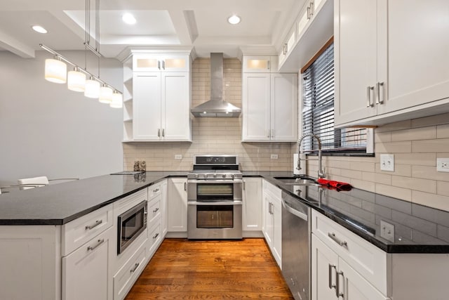 kitchen featuring a peninsula, a sink, wall chimney range hood, appliances with stainless steel finishes, and open shelves