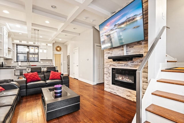 living room featuring dark wood-style flooring, beam ceiling, a stone fireplace, coffered ceiling, and stairs