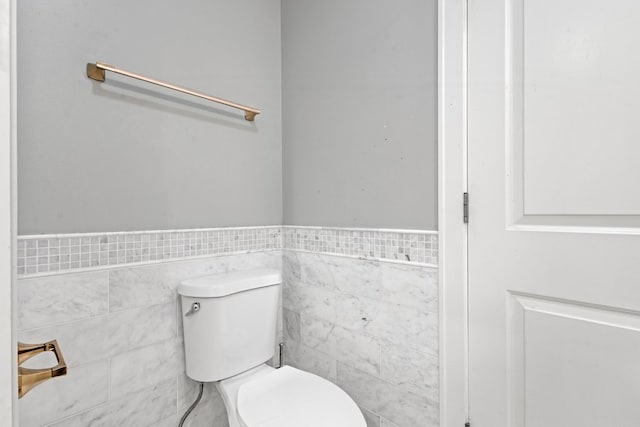 bathroom featuring a wainscoted wall, tile walls, and toilet