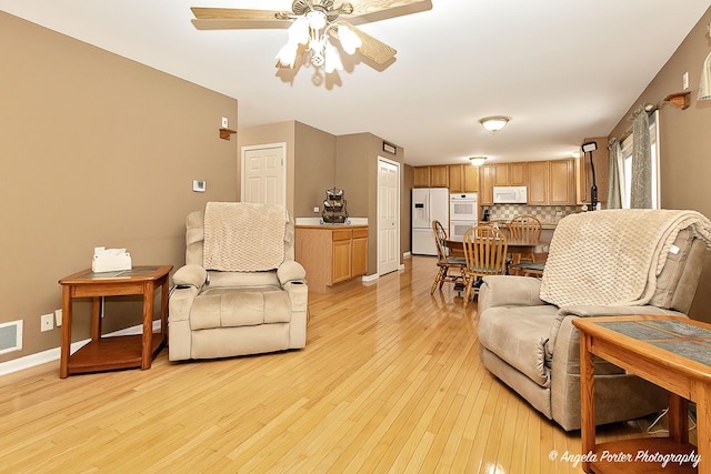 living room featuring light wood finished floors, a ceiling fan, visible vents, and baseboards