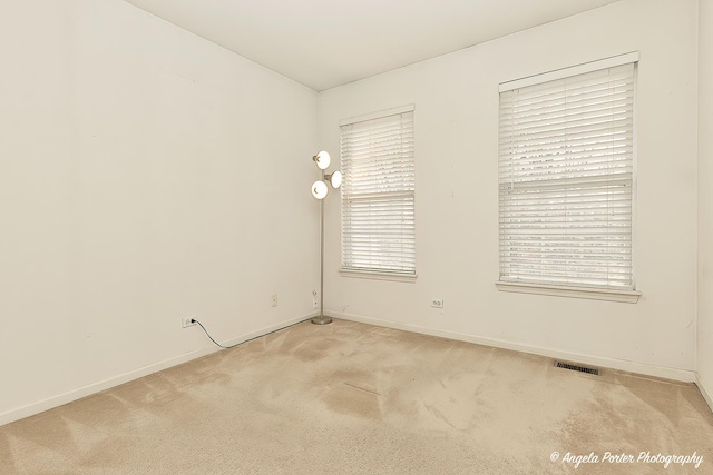 spare room with light colored carpet, visible vents, plenty of natural light, and baseboards