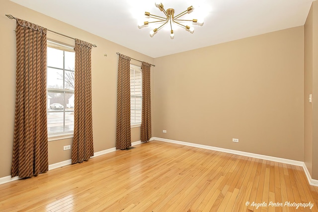 unfurnished room with light wood-type flooring, a notable chandelier, and baseboards