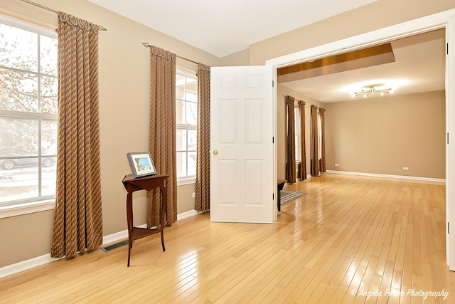 spare room with light wood-type flooring, visible vents, and baseboards