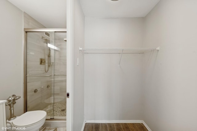 bathroom with a stall shower, wood finished floors, toilet, and baseboards