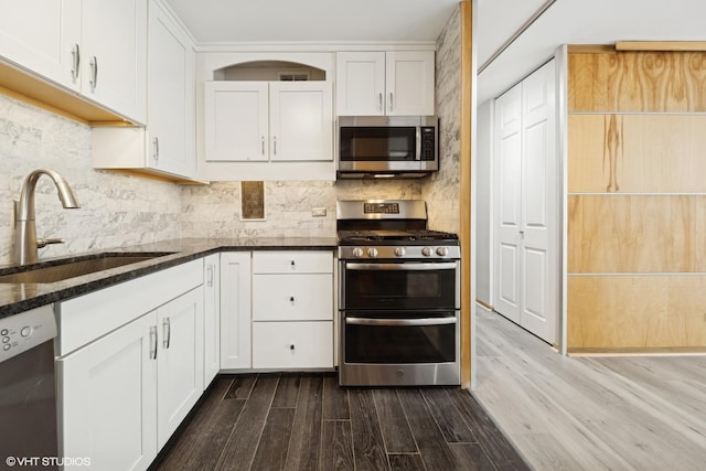 kitchen with appliances with stainless steel finishes, dark stone counters, a sink, and backsplash