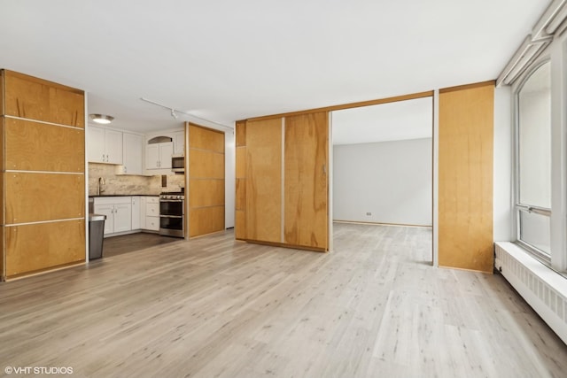 unfurnished living room featuring track lighting, light wood-type flooring, a sink, and radiator heating unit