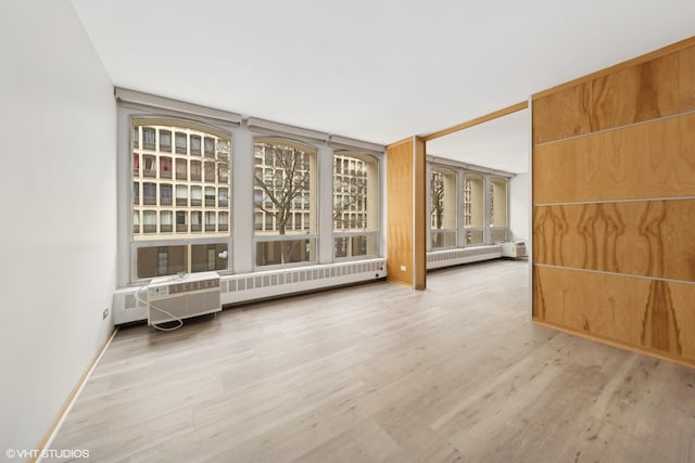 unfurnished room with radiator heating unit, baseboards, wood finished floors, and a wall mounted air conditioner