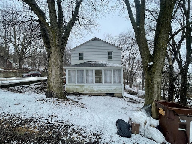 snow covered back of property with a sunroom