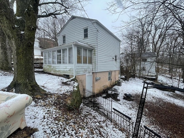 snow covered property with a sunroom, fence, and central AC unit