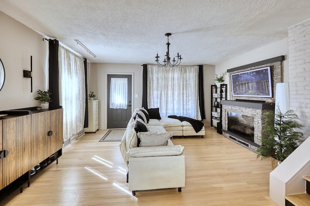 living room featuring a textured ceiling, a chandelier, a fireplace, and light wood finished floors