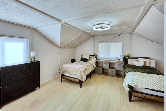 bedroom with light wood-style floors, multiple windows, a textured ceiling, and vaulted ceiling