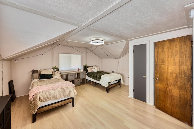 bedroom with vaulted ceiling, light wood-style flooring, and a textured ceiling