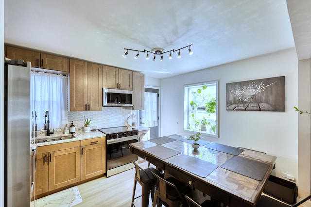 kitchen featuring brown cabinets, a sink, appliances with stainless steel finishes, light wood finished floors, and decorative backsplash