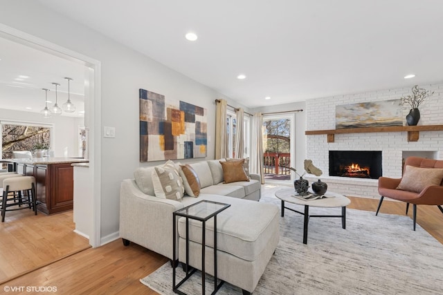 living area with recessed lighting, a brick fireplace, light wood-type flooring, and baseboards