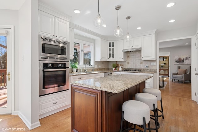 kitchen featuring a breakfast bar, under cabinet range hood, a sink, backsplash, and appliances with stainless steel finishes