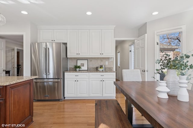 kitchen featuring backsplash, light stone countertops, high end refrigerator, light wood-style floors, and white cabinetry