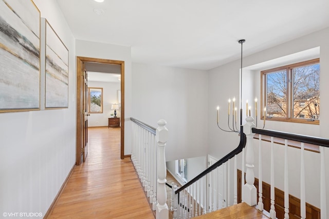 corridor with light wood-style flooring, an upstairs landing, baseboards, and a chandelier