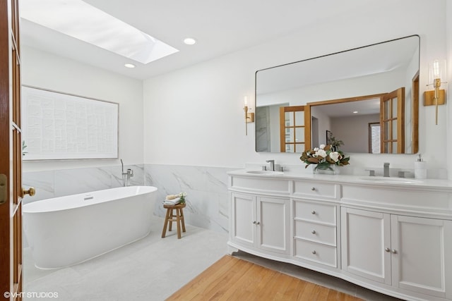 full bathroom featuring a sink, a soaking tub, a skylight, and double vanity