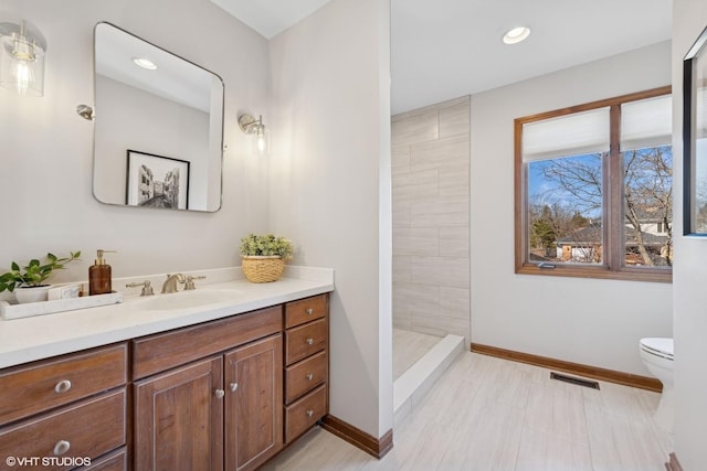 bathroom featuring visible vents, baseboards, toilet, tiled shower, and vanity