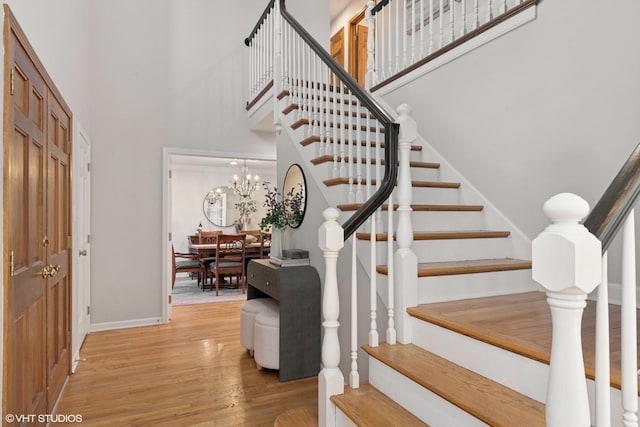 stairway with an inviting chandelier, a high ceiling, baseboards, and wood finished floors