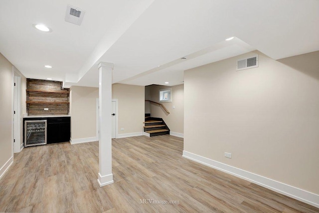 finished basement featuring stairway, beverage cooler, visible vents, and light wood finished floors