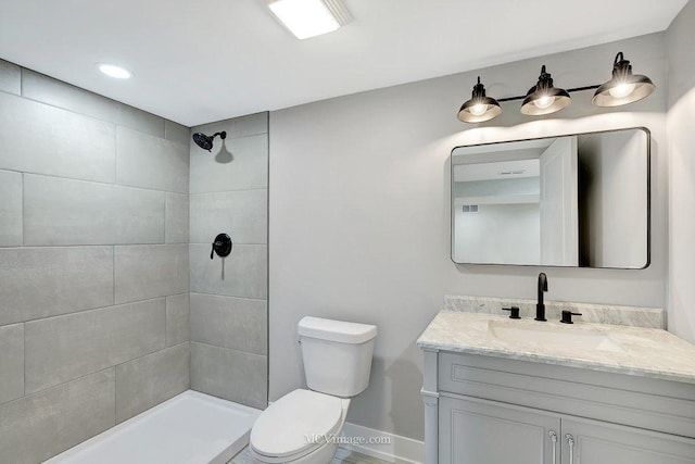 bathroom featuring toilet, baseboards, a tile shower, and vanity