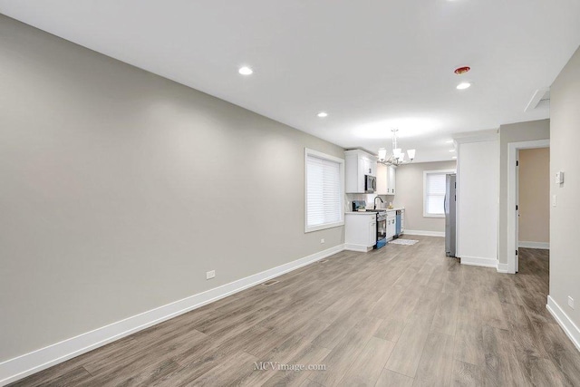 unfurnished living room featuring baseboards, recessed lighting, an inviting chandelier, and light wood-style floors