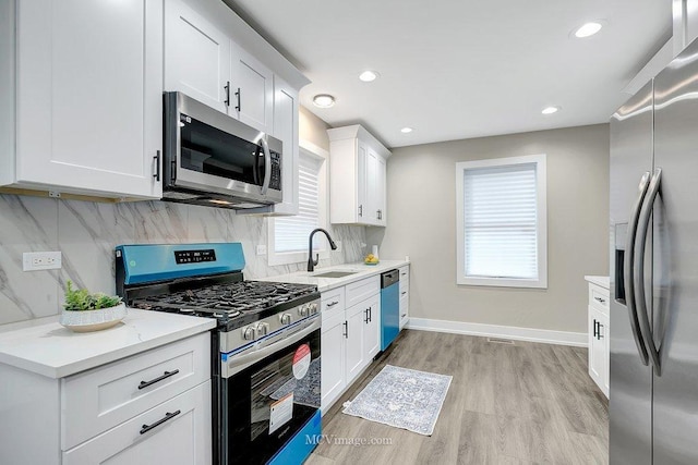 kitchen with baseboards, appliances with stainless steel finishes, light countertops, light wood-type flooring, and backsplash