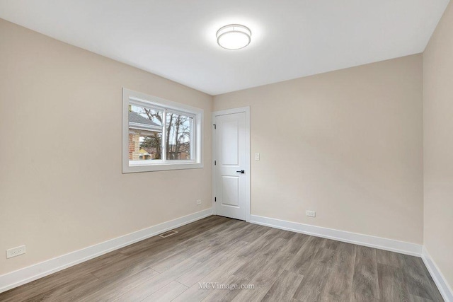 empty room featuring wood finished floors, visible vents, and baseboards