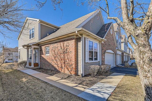 view of side of home with brick siding, roof with shingles, an attached garage, and aphalt driveway