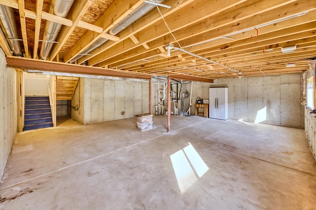 unfinished basement featuring stairway and freestanding refrigerator