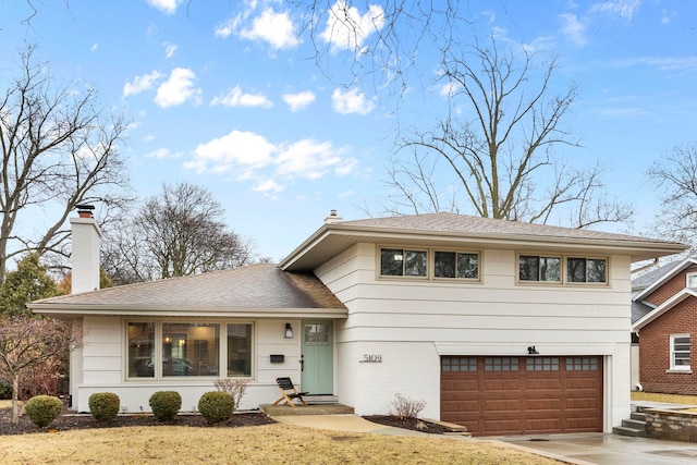 split level home with brick siding, an attached garage, concrete driveway, and a chimney