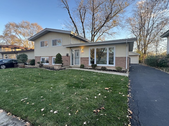 tri-level home with a garage, brick siding, and a front lawn