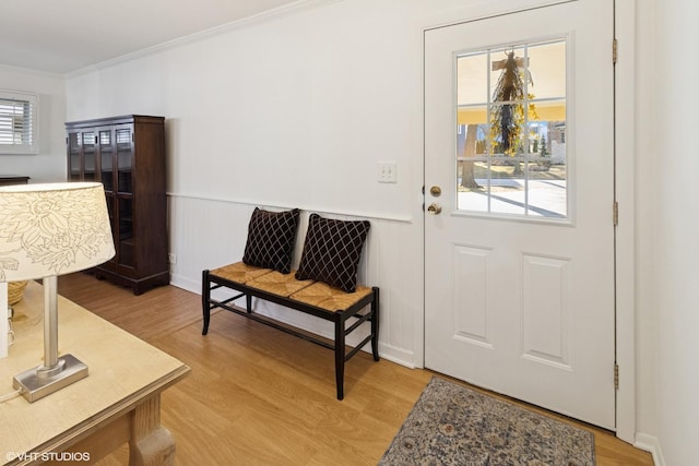 foyer with a wainscoted wall, light wood-style flooring, and ornamental molding