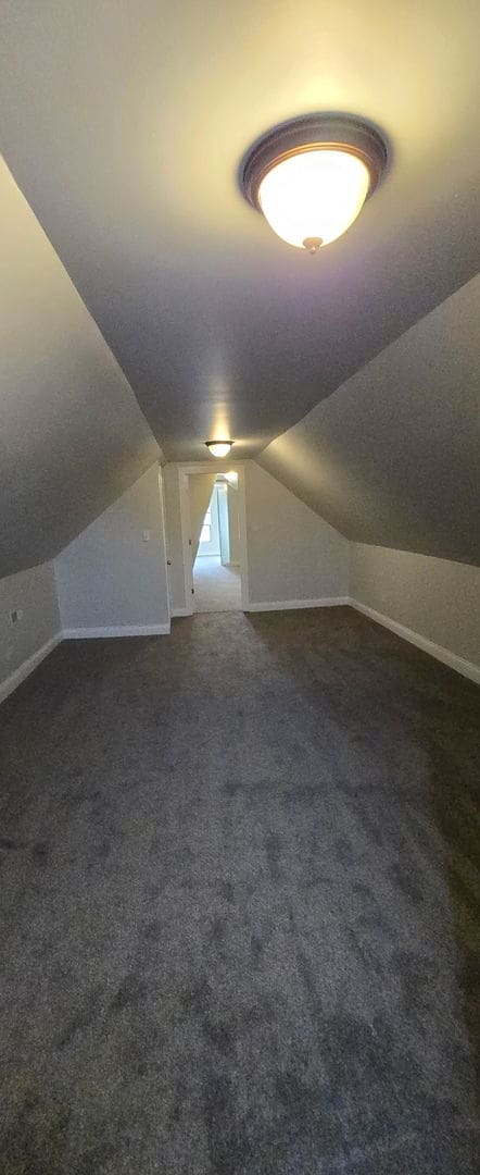 bonus room with lofted ceiling, dark carpet, and baseboards